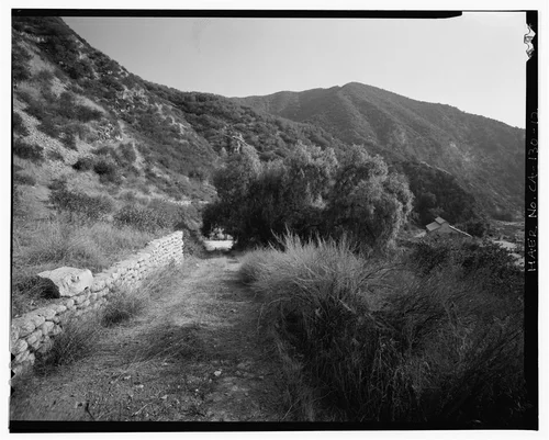  OVERVIEW FROM FORMER RESIDENTIAL AREA NORTH OF SAR-2, SHOWING TRAIL UP TO FOREBAY, RETAINING WALL, PEPPER TREES, AND SAR-2 IN DISTANCE. VIEW TO SOUTH-SOUTHEAST. - Santa Ana River Hydroelectric System, Redlands, San Bernardino County, CA