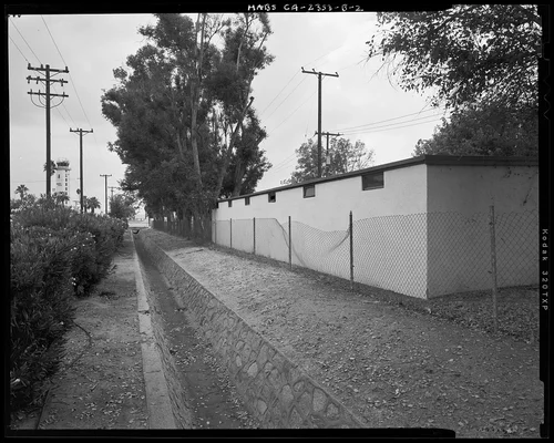 CONTEXTUAL VIEW SHOWING NORTHEAST CORNER OF BUILDING 257 WITH MARCH FIELD HISTORIC DISTRICT STONE DRAINAGE CANAL TO EAST - March Air Force Base, March Field, Garage, East side of L Street north of X Street, Moreno Valley, Riverside County, CA