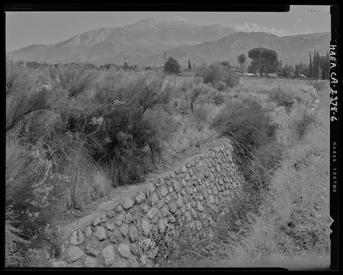 View of middle section of channel, showing east face of the channel rock wall, looking downstream; looking east-southeast. - Gilman Canyon Storm Drain, Banning Bench to North 8th & West Nicolet Streets, Banning, Riverside County, CA