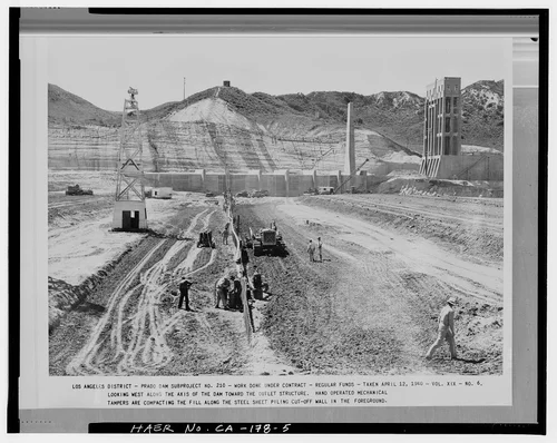  LOOKING WEST ALONG THE AXIS OF THE DAM TOWARD THE OUTLET STRUCTURE. HAND OPERATED MECHANICAL TAMPERS ARE COMPACTING THE FILL ALONG THE STEEL SHEET PILING CUTOFF WALL IN THE FOREGROUND. Volume XIX, No. 6, April 12, 1940. - Prado Dam, Santa Ana River near junction of State Highways 71 & 91, Corona, Riverside County, CA