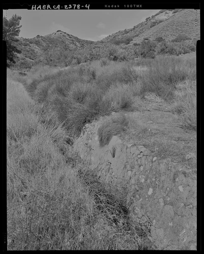 Contextual view at the northern channel section immediately downstream from channel mouth showing the east face of the channel rock wall, looking upstream to the northwest. - Gilman Canyon Storm Drain, Banning Bench to North 8th & West Nicolet Streets, Banning, Riverside County, CA