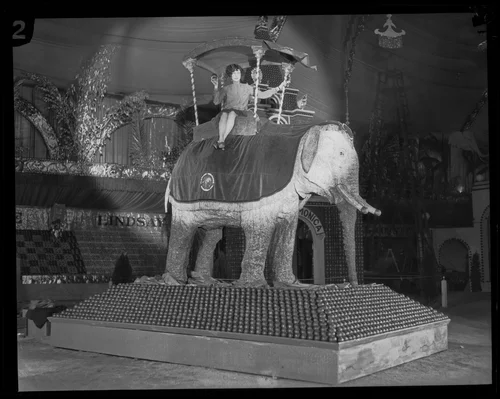 Woman sits atop an elephant-shaped display at the National Orange Show, San Bernardino, 1926
