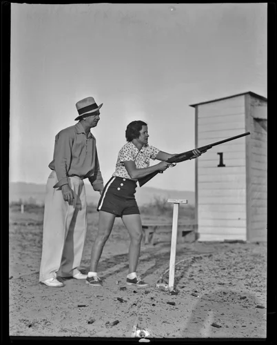 Mrs. Luke holds a gun with Carl Bradsher stands behind her, Palm Springs, 1936