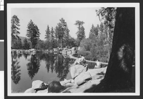 Two women and a man seated on rocks overlooking Bartlett's Cedar Lake near Big Bear Lake, ca.1950